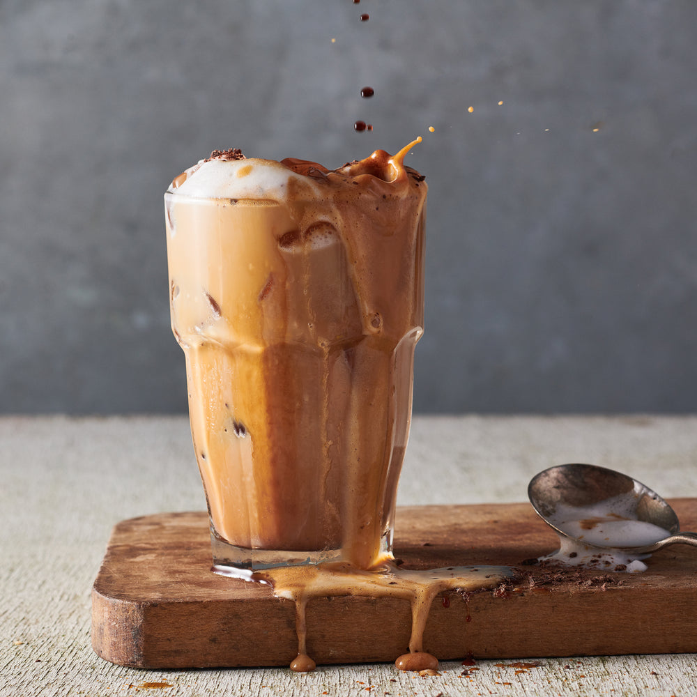 Kohana coffee cold brew mocha frappe in a glass on a table with a spoon next to it
